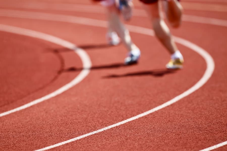 Two runners rounding curve of red surface running track