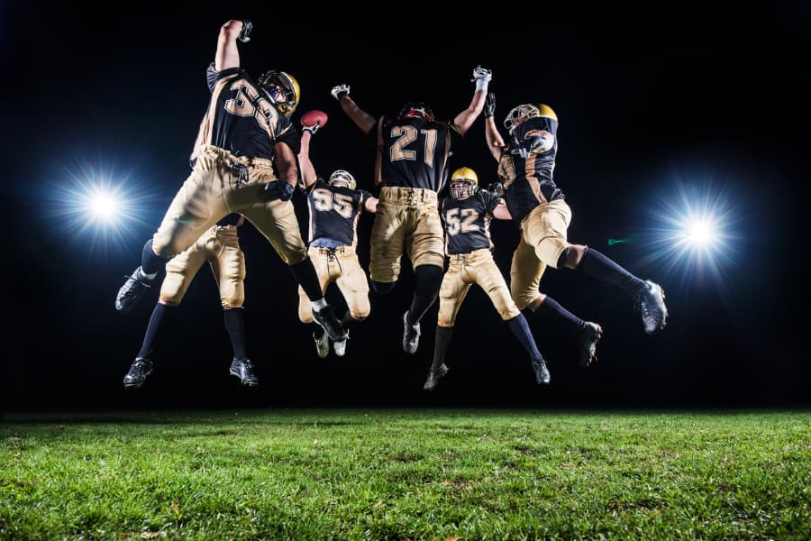 Group of football players on turf football field celebrate by jumping into the air