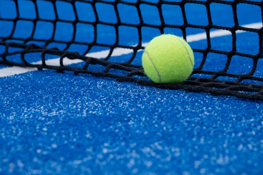 Tennis ball resting on net of tennis court