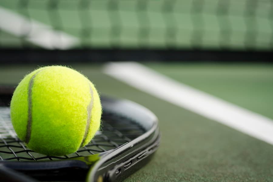 Tennis ball on top of racket that’s resting on asphalt court