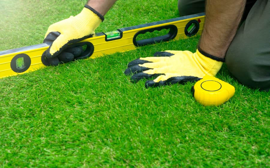 Worker inspecting artificial turf field and checking tilt with level